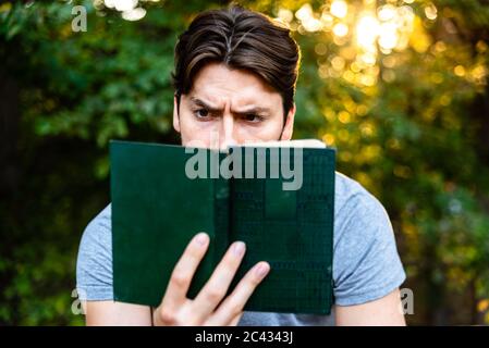 Junger Mann liest eine self-centered Roman in einem Park bei Sonnenuntergang sitzen, genießen der antiken Literatur. Stockfoto
