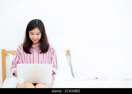 Schöne Porträt freiberufliche asiatische junge Frau sitzen entspannen und Freizeit arbeiten Laptop-Computer Internet online auf Bett im Schlafzimmer, fröhlich asien Mädchen Stockfoto