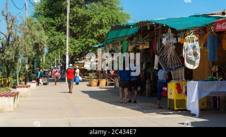 Mancora, Piura / Peru - April 10 2019: Touristen, die in der Gegend der Kunsthandwerkshändler entlang der Hauptstraße der Stadt mit dem Leuchtturm im Hintergrund spazieren gehen Stockfoto