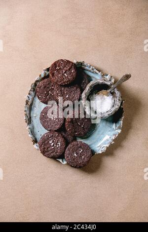 Hausgemachte dunkle Schokolade gesalzene Brownies Kekse mit Salzflocken in blauen Keramikplatte über braunen Textur Hintergrund. Flach, Platz Stockfoto