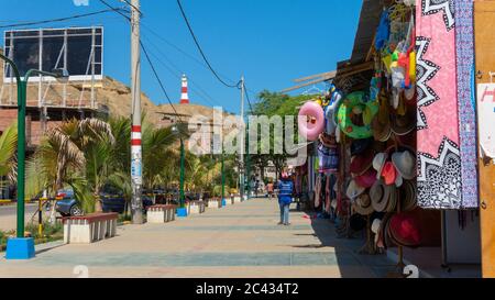 Mancora, Piura / Peru - April 10 2019: Touristen, die in der Gegend der Kunsthandwerkshändler entlang der Hauptstraße der Stadt mit dem Leuchtturm im Hintergrund spazieren gehen Stockfoto