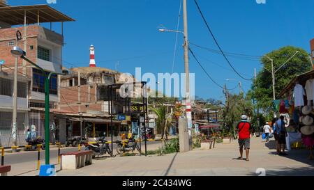 Mancora, Piura / Peru - April 10 2019: Touristen, die in der Gegend der Kunsthandwerkshändler entlang der Hauptstraße der Stadt mit dem Leuchtturm im Hintergrund spazieren gehen Stockfoto