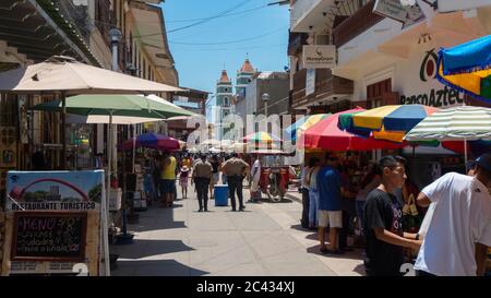 Catacaos, Piura / Peru - 6. April 2019: Touristen gehen auf einer Straße voller Handwerksbetriebe im Zentrum der Stadt mit der Kirche im Hintergrund Stockfoto