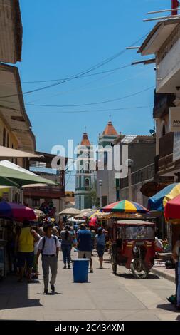 Catacaos, Piura / Peru - 6. April 2019: Touristen gehen auf einer Straße voller Handwerksbetriebe im Zentrum der Stadt mit der Kirche im Hintergrund Stockfoto