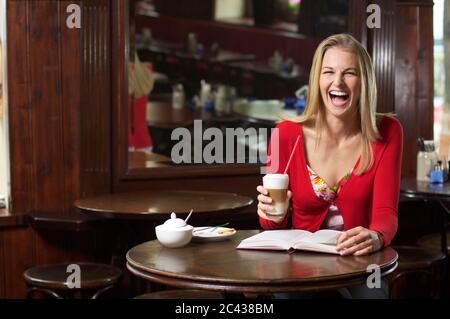 Frau hält ein Glas Latte Macchiato in einem Café und lacht Stockfoto