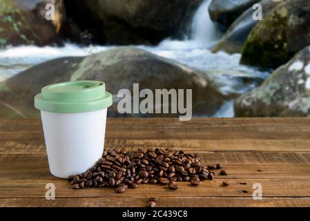 Kaffeebecher mit Bohnen neben dem Tisch in der Nähe des Wasserfalls Stockfoto