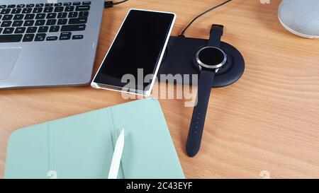 Mobiltelefon und Smart Watch auf einem dualen kabellosen Ladegerät mit Tablet und Stylus-Konzept für drahtlose Technologie und tragbare Informationsgeräte Stockfoto