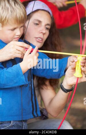 Frau hilft einem Jungen mit Pfeil und Bogen Stockfoto