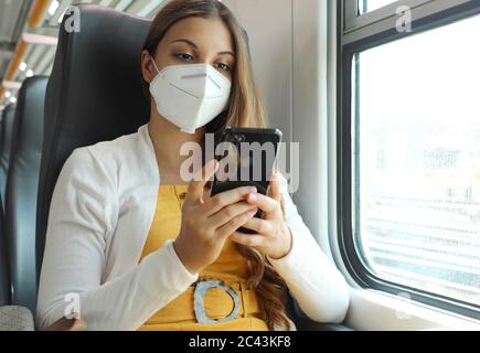 Entspannte Frau mit KN95 FFP2 Gesichtsmaske mit Smartphone-App. Zug Passagier mit Schutzmaske reisen in Business-Klasse SMS auf mobi sitzen Stockfoto