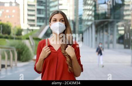 Junge Frau trägt Schutzmaske KN95 FFP2 zu Fuß in der modernen Stadt Straße. Studentin mit Gesichtsmaske gegen Coronavirus-Krankheit 2019 (COVID-19). Stockfoto