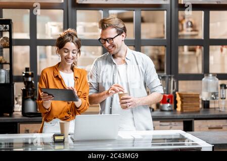 Zwei junge Manager oder Ladenbesitzer, die sich mit einem digitalen Tablet am Ladentisch oder Café mit einem Gespräch herumsprechen. Management-Konzept für kleine Unternehmen Stockfoto