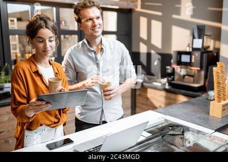 Zwei junge Manager oder Ladenbesitzer, die sich mit einem digitalen Tablet am Ladentisch oder Café mit einem Gespräch herumsprechen. Management-Konzept für kleine Unternehmen Stockfoto