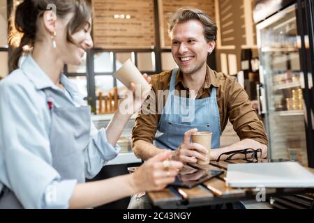 Ein paar junge Cafe-Arbeiter haben einige Geschäftsgespräche, während sie mit Kaffee am Tisch ihres Cafés oder Konditorei sitzen Stockfoto