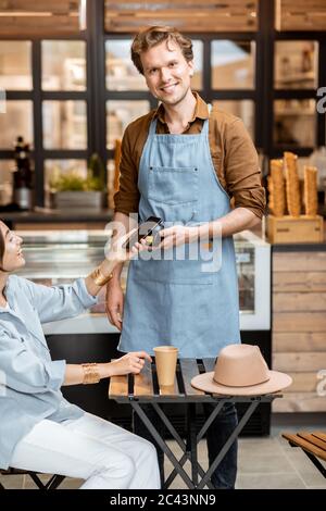 Glücklicher Kellner mit einem Kunden im Café oder Eisdiele, kontaktlose Bezahlung mit einem Smartphone Stockfoto