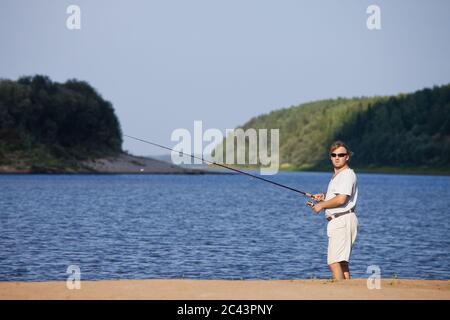 Ein Fischer mit einer Spinnrute am Flussufer Stockfoto