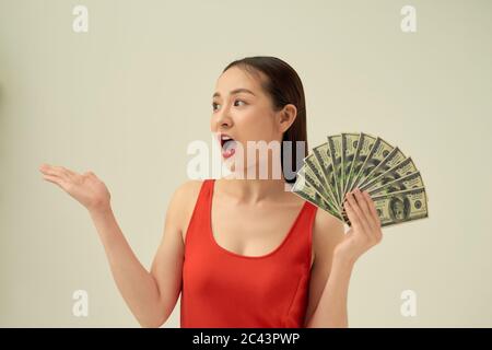 Porträt einer aufgeregt schönen jungen Frau, die isoliert über hellem Hintergrund steht und Geldscheine zeigt Stockfoto