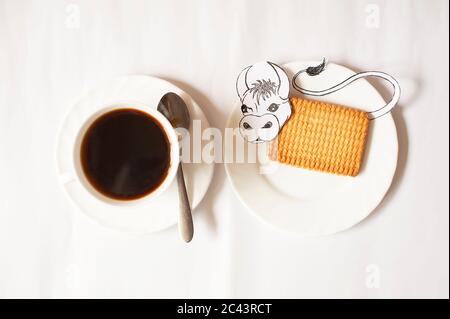 Foto einer Tasse Kaffee mit einem rechteckigen Keks und einem bemalten Stier auf weißem Hintergrund Stockfoto