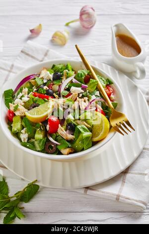 Nahaufnahme von gezupftem Hühnerfleisch, Oliven, roten Zwiebeln, Tomaten, Gurke, Minze, Salat mit zerbröseltem Fetakäse in einer weißen Schüssel, verti, bestreut Stockfoto