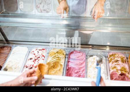 Verkäufer pflücken Eis mit einem Löffel aus dem Kühlschrank im Geschäft. Blick von oben auf ein Tablett voller Eis mit verschiedenen Geschmacksrichtungen Stockfoto