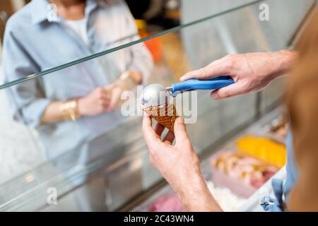 Verkäufer, der Eisbälle in den Waffelkegel setzt und Süßigkeiten für eine junge Frau in einem Geschäft verkauft Stockfoto