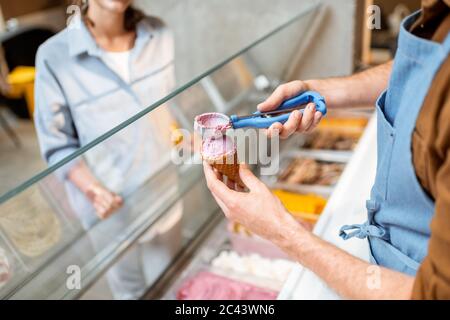 Verkäufer, der Eisbälle in den Waffelkegel setzt und Süßigkeiten für eine junge Frau in einem Geschäft verkauft Stockfoto