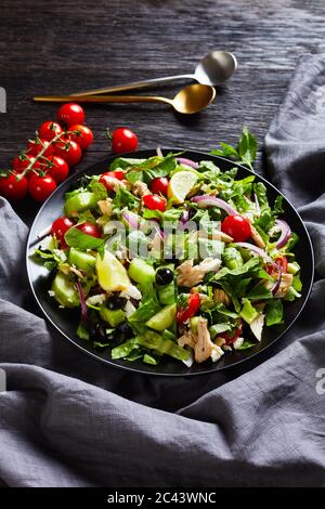 Salat mit gezupftem Hühnerfleisch, Oliven, roten Zwiebeln, Tomaten, Gurken, Minze, Salat, bestreut mit zerbröseltem Feta-Käse in einer schwarzen Schüssel, vertikale Ansicht Stockfoto