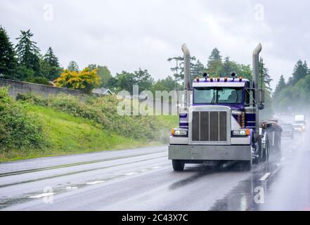 Leistungsstarke klassische industrielle Qualität große Rig blau semi-Truck mit hohen Auspuffrohren und Flachbett Sattelauflieger läuft auf der Gefahr nass regnet Straße wit Stockfoto