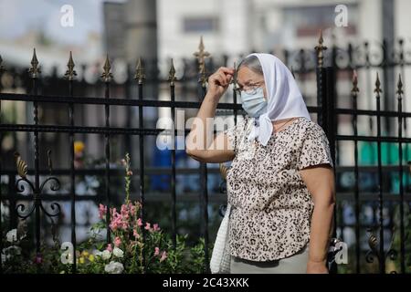 Snagov, Rumänien - 21. Juni 2020: Ältere Frau mit Covid-19 Maske betet vor einer orthodoxen christlichen Kirche. Stockfoto