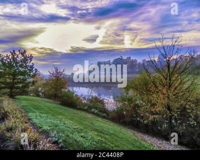 Ein Bild eines kleinen Teiches, umgeben von Vegetation, an einem Herbst/Herbstmorgen. Eine dünne Wolkenschicht bedeckt die Sonne, wenn sie aus dem Osten aufsteigt. Stockfoto