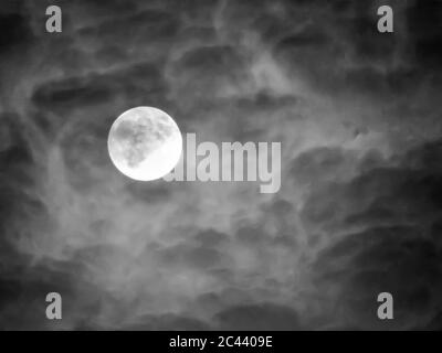 Eine dünne Wolkenschicht bedeckt einen Vollmond. Das reflektierte Licht des Mondes und die Schatten der Wolken geben ihm einen sehr unheimlichen/unheimlichen Effekt. Stockfoto