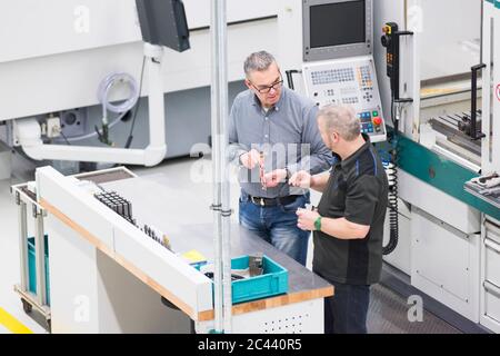 Zwei Männer, die in einer Fabrik an einer Maschine sprechen Stockfoto