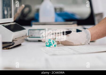 Nahaufnahme einer Technikerin, die einen Becher mit Tabletten auf dem Schreibtisch im Labor hält Stockfoto