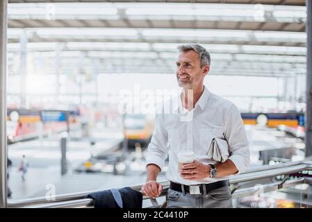 Ein nachdenklicher Geschäftsmann hält Kaffee und schaut beim Geländer stehen Stockfoto