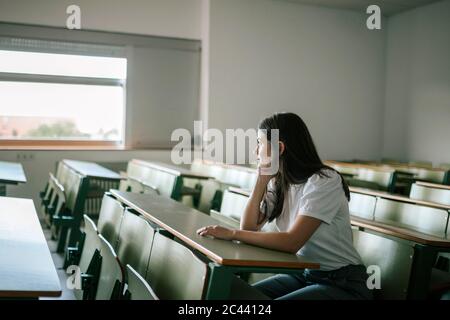 Nachdenkliche junge Frau, die beim Sitzen am Schreibtisch wegschaut Stockfoto