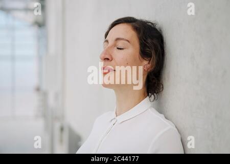 Porträt einer Geschäftsfrau mit geschlossenen Augen, die an einer Betonwand lehnt Stockfoto