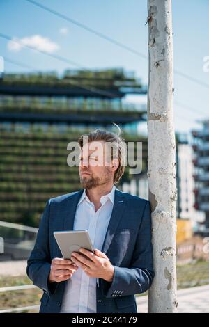 Geschäftsmann lehnt sich an Baumstamm in der Stadt mit Tablet Stockfoto