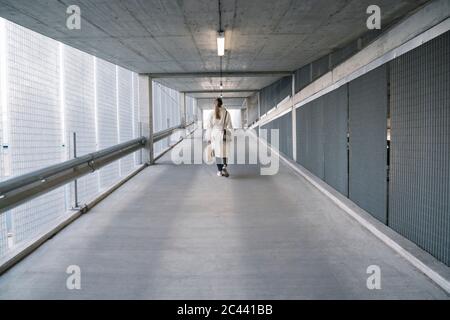 Rückansicht einer Frau, die nach dem Einkaufen im Korridor eines Parkplatzes läuft Stockfoto