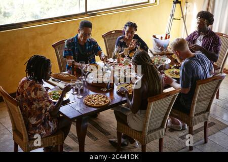 Blick auf Freunde, die beim Essen am Esstisch sitzen und das Mittagessen genießen Stockfoto