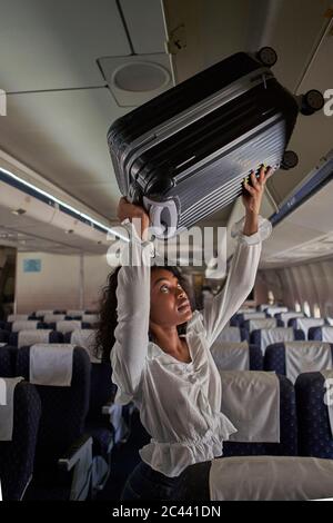 Junge Frau, die Gepäck im Stauraum im Flugzeug positioniert Stockfoto