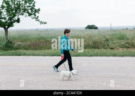 Rückansicht einer älteren Frau, die mit ihrem Hund auf dem Land spazieren geht Stockfoto