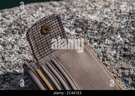 Details und Elemente von handgefertigten Geldbörse aus braunem Leder und kariertem Textil auf Steinhintergrund. Herrenaccessoire. Stockfoto