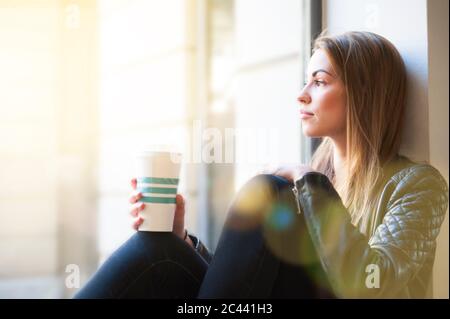 Frau schaute durch das Fenster, während sie im Café die Einweg-Kaffeetasse hielt Stockfoto