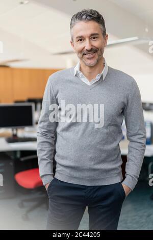 Porträt eines lächelnden, gutaussehenden Geschäftsmannes, der mit Händen in den Taschen im Büro steht Stockfoto