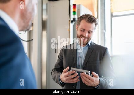 Lächelnder junger Geschäftsmann in einer Fabrik, die Werkstück hält Stockfoto