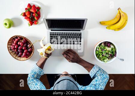 Mann, der beim Essen am Schreibtisch im Heimbüro arbeitet Stockfoto