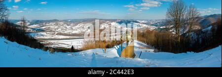 Kapelle auf der Höhe des Berges im Winter mit einem herrlichen Panorama von Gipfeln und Wald unter dem klaren Himmel Stockfoto