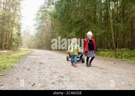 Zwei kleine Schwestern ziehen Trolley auf Waldweg Stockfoto