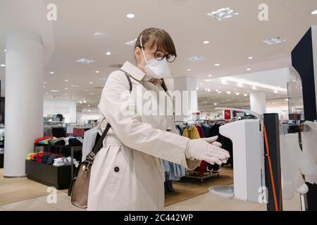 Frau mit Gesichtsmaske und Einweghandschuhe Desinfektion ihrer Hände vor dem Einkaufen in einem Modehaus Stockfoto