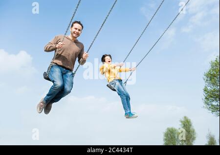 Fröhlicher Vater und Sohn schwingen gegen blauen Himmel Stockfoto