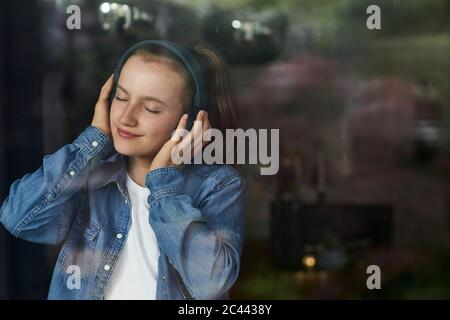 Mädchen mit geschlossenen Augen, die Musik hören, die über Kopfhörer zu Hause Stockfoto